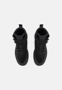 Para czarnych wysokich sneakerów z grubymi podeszwami i wyściełanymi kołnierzami, widok z góry na jasnoszarym tle.