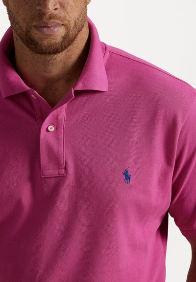 Koszulka polo w intensywnym różowym kolorze, wykonana z bawełnianego materiału o fakturowanej powierzchni, z dwu guzikowym zapięciem i niebieskim haftowanym logo na piersi.