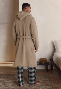 Beez värvi kapuutsiga hommikumantel, mis on vöödiga puusa ümber, koos musta ja valge ruudulise pidžaamapükstega. Villane tekstuur, mugav lõige.