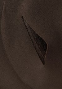 Hnědý textil se hladkým povrchem má trojúhelníkový výřez, který odhaluje síťovou vrstvu pod ním a zdůrazňuje jeho vrstvený design.
