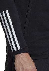 Schwarzes, athletisches Langarmshirt mit einem weißen Drei-Streifen-Design auf dem Ärmel, gefertigt aus einem glatten, dehnbaren Stoff.