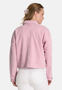 Rosa verkürzte Jeansjacke mit strukturiertem Kragen und sichtbaren Nahtdetails. Der Stoff hat eine weiche Textur und einen lässigen Schnitt.