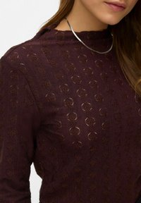 Vinröd texturerad topp med ett upphöjt mönster i form av diamantformer. Har en hög hals och kompletteras med ett silverhalsband.