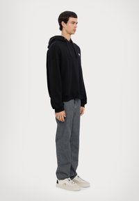 Schwarzer Kapuzenpullover mit lockerem Schnitt und gerippten Bündchen, kombiniert mit grauen Jeans und weißen Sneakers mit schwarzen Akzenten.