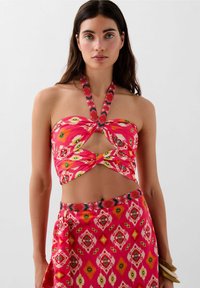Completo a due pezzi composto da un top corto rosa a fascia con un taglio e un motivo floreale, abbinato a una gonna coordinata con una stampa geometrica.