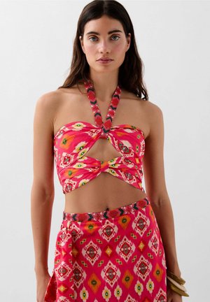 Completo a due pezzi composto da un top corto rosa a fascia con un taglio e un motivo floreale, abbinato a una gonna coordinata con una stampa geometrica.