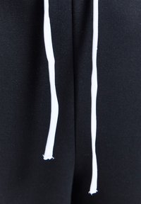 Ţesătură neagră cu două șnururi albe care atârnă în jos, ușor destrămate la capete.