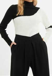 Jersey de cuello alto acanalado en blanco y negro con bloques de color asimétricos, diseño entallado y mangas largas. Combinado con pantalones negros de talle alto.