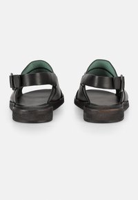 Sandali neri in pelle con suola piatta, apertura sul retro e cinturino regolabile con fibbia. Interno foderato in verde per un contrasto aggiuntivo.