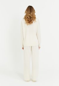 Maglione a maglia color crema e pantaloni larghi coordinati, con una vestibilità comoda e una consistenza morbida, visti dal retro su uno sfondo bianco.
