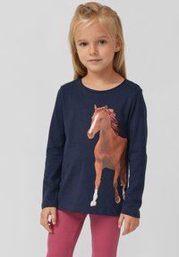 Navyblaues Langarm-Chemise aus Baumwolle mit einem großen Pferde-Motiv in Brauntönen. Getragen mit gerippten pinken Leggings. Schlichter runder Ausschnitt.