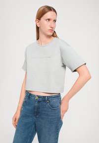 Gray cropped t-shirt with a round neckline and short sleeves, featuring embossed "Michael Kors" branding. Paired with high-waisted blue denim jeans.