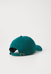 Teal baseball cap made of cotton, featuring a curved visor, adjustable strap with a metal buckle, and six ventilation eyelets.