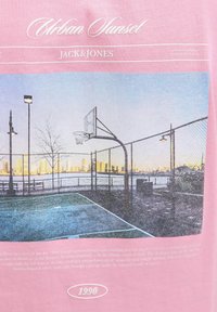Rožinė marškinė su spauda, vaizduojančia krepšinio aikštelę saulėlydyje, kurioje matosi krepšinio lankas, grandininė tvora ir miesto panorama švelniomis spalvomis.