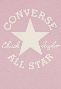 Ροζ μπλουζάκι με έντονο λευκό αστέρα και το κείμενο "CONVERSE Chuck Taylor ALL STAR" σε διάφορα στυλ γραμματοσειρών.