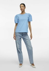 Jasnoniebieski bawełniany t-shirt z bufkami z koronkowymi detalami, w połączeniu z jasnoniebieskimi dżinsami i białymi czółenkami.