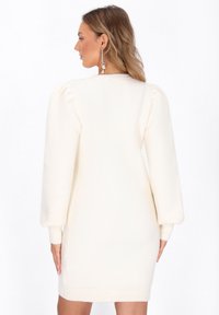 Valkoinen neulemekko, jossa on vartalonmyötäinen siluetti, puffihihat, ribbed-hihansuut ja pehmeä kangas, sopii rentoon käyttöön.