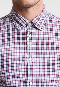 Rutigt skjort med knappar i vitt, rött och marinblå mönster; klassisk krage, korta ärmar och slät tygtextur.