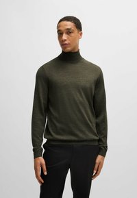 Maglione a collo alto verde scuro con maniche lunghe, realizzato in un materiale morbido e testurizzato. Presenta un collo aderente e polsini a coste per un comfort aggiuntivo.