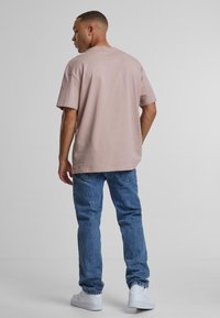 Vaaleanpunainen puuvillainen t-paita lyhyillä hihoilla, rento muotoilu ja pyöreä kaula-aukko, päällä siniset denim-farkut ja valkoiset lenkkarit.
