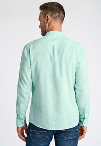 Camicia a maniche lunghe verde menta con colletto a button-down, tessuto con texture e dettagli sul retro, abbinata a jeans di denim blu.