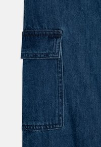 Mörkblå denimtyg med en sidoficka med lock, dubbla sömmar och en lätt texturerad yta. Ren design utan synliga varumärkesloggor.