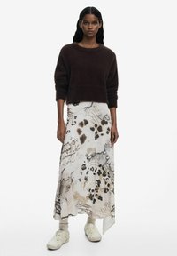 Maglione marrone peloso abbinato a una lunga gonna a fantasia con design astratti beige, neri e marroni, completato da calzature chiare.