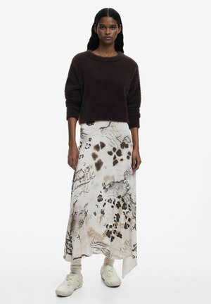 Maglione marrone peloso abbinato a una lunga gonna a fantasia con design astratti beige, neri e marroni, completato da calzature chiare.