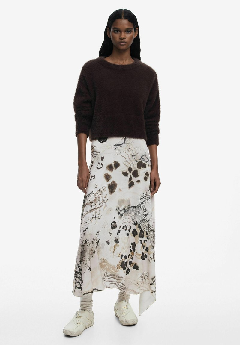 Maglione marrone peloso abbinato a una lunga gonna a fantasia con design astratti beige, neri e marroni, completato da calzature chiare.
