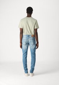 Ljust blå skinny jeans i denim med en blekt struktur, kombinerat med en ljusgrön t-shirt. Har en brun lädermärke.