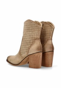 Botines beige con un diseño superior perforado, material de ante texturizado y un tacón de madera apilada. Presentan un cierre con cremallera en el costado.