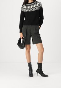 Svart stickad tröja med vit mönstrad ok, grå skräddarsydda shorts, svarta ankelstövlar och en svart handväska. Enkel, modern design.