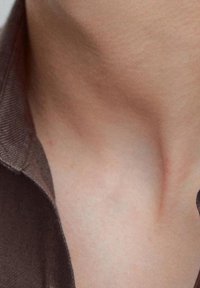 Brauner Hemdkragen aus Stoff, der sich über glatte Hauttöne legt, und eine strukturierte Stoffoberfläche mit subtilen Konturen im Halsbereich zeigt.