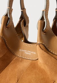 Brązowa skórzana torebka z gładkim wykończeniem i zamszowymi akcentami. Posiada przeszywane detale oraz metkę z logo. Uchwyty mają metalowy element.