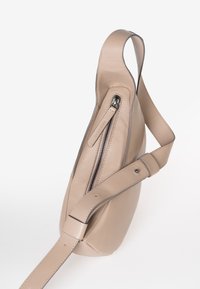 Beige leren schoudertas met een verstelbare strap en een voorvak met ritssluiting, weergegeven tegen een witte achtergrond.