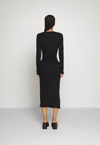 Musta pitkähihaine mekko, jossa on rypytettyä yksityiskohtaa sivuilla, keskipituinen, valmistettu sileästä, venyvästä kankaasta, yhdistettynä paksupohjaisiin sandaaleihin.