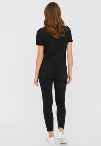 Svart bomull T-skjorte med rund hals, kombinert med svarte skinny jeans. Modell som har på seg hvite sneakers. Glatt tekstur med en avslappet passform.