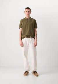 Oliven grøn polo shirt med korte ærmer, hvide løse bukser og brune ruskinds sko med snørebånd. Simpel design, minimale detaljer.