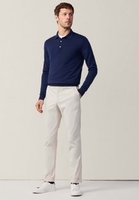 Granatowa koszulka polo z długim rękawem i zapięciem na guziki, w zestawieniu z białymi slim-fit spodniami i białymi trampkami. Gładka tekstura, casualowy design.