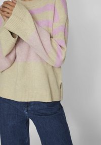 Beige stickad tröja med rosa horisontella ränder, ribbade ärmslut och nederkant. Har en avslappnad passform och sidofickor för ökad rörlighet.