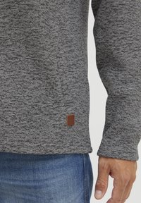 Maglione grigio a maglia con un motivo testurizzato, dotato di una piccola etichetta in pelle marrone vicino all'orlo e un design delle maniche a vestibilità rilassata.