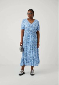 Μπλε φορεμάκι midi με κοντά φουσκωτά μανίκια, V-cut, συγκεντρωμένη μέση, φαρδιά στρίφωμα και διακριτικές ρίγες. Συνδυάζεται με μεταλλικές μπότες brogue και μια μικρή τσάντα.