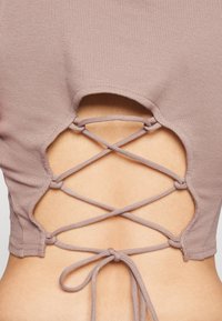 Prążkowany różowy top crop z wycięciem na plecach, z krzyżującymi się wiązaniami oraz wiązaniem na dole. Miękka, strukturalna tkanina.