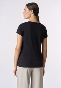 T-shirt nera a maniche corte con scollo rotondo, in morbido cotone e vestibilità comoda, abbinata a pantaloni larghi color beige chiaro.