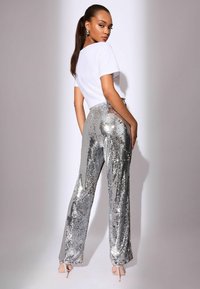 Wysokie, srebrne spodnie z cekinami o rozszerzanym kroju, zestawione z dopasowaną, białą bluzką z krótkim rękawem; błyszcząca faktura i odblaskowe akcenty.