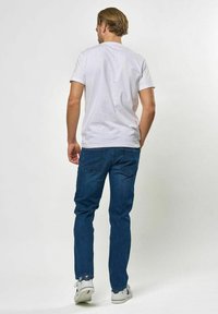 Fehér rövid ujjú póló sötétkék farmerrel párosítva. A farmer klasszikus fazonú hátsó zsebekkel, a megjelenést fehér tornacipő teszi teljessé.