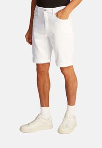 Pantalones cortos de mezclilla blanca con dobladillos enrollados, diseño de cinco bolsillos y cierre de botón metálico, combinados con zapatillas blancas y calcetas blancas.