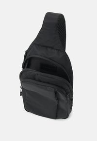Černá látková taška přes rameno s texturovaným popruhem, zipovými přihrádkami a plochou přední kapsou. Obsahuje hladké zipy a minimalistický design.