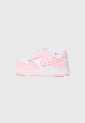 Baskets Nike avec une tige en cuir blanc et des accents roses, bout rond, laçage et épaisse semelle en caoutchouc texturée.