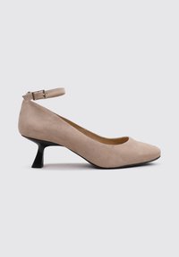 Escarpin à bride de cheville en suède beige avec un bout rond et un talon noir effilé. Le design présente une texture lisse et un minimum de détails.